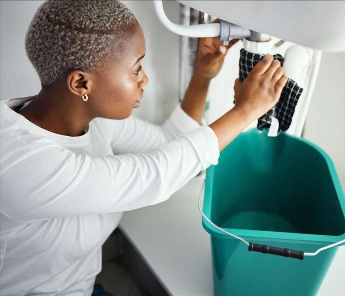 Plumbing, water and a woman in the bathroom of her home with a cloth and bucket waiting for assistance.